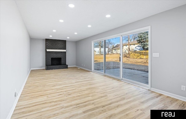 unfurnished living room with recessed lighting, a brick fireplace, light wood-style flooring, and baseboards