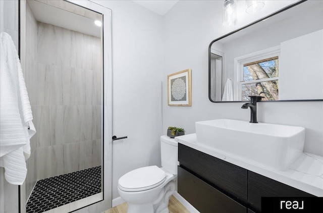 bathroom featuring a tile shower, vanity, and toilet