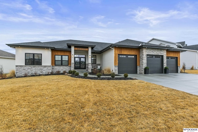 prairie-style house with an attached garage, a shingled roof, stone siding, driveway, and a front lawn