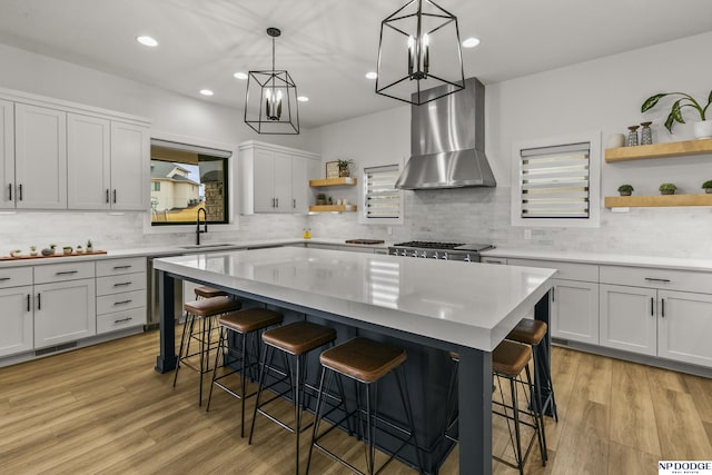 kitchen featuring open shelves, a breakfast bar area, wall chimney exhaust hood, and light countertops