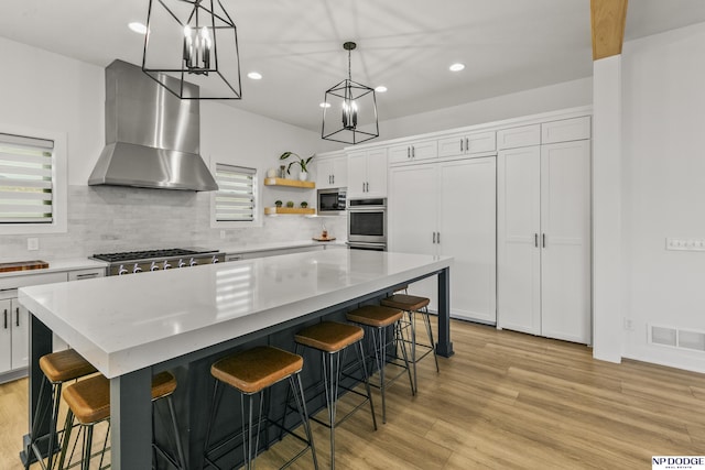 kitchen with stainless steel appliances, visible vents, light wood-style flooring, white cabinets, and wall chimney range hood