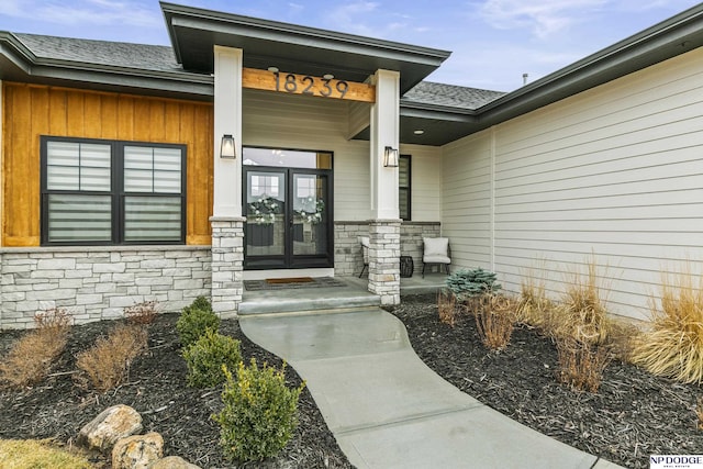 property entrance with stone siding, french doors, roof with shingles, and covered porch