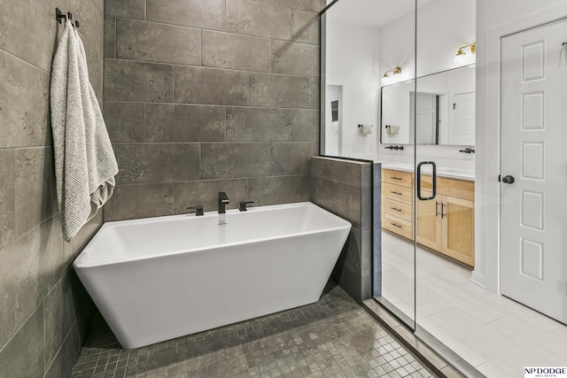 full bath with a soaking tub, vanity, tile walls, and tile patterned floors