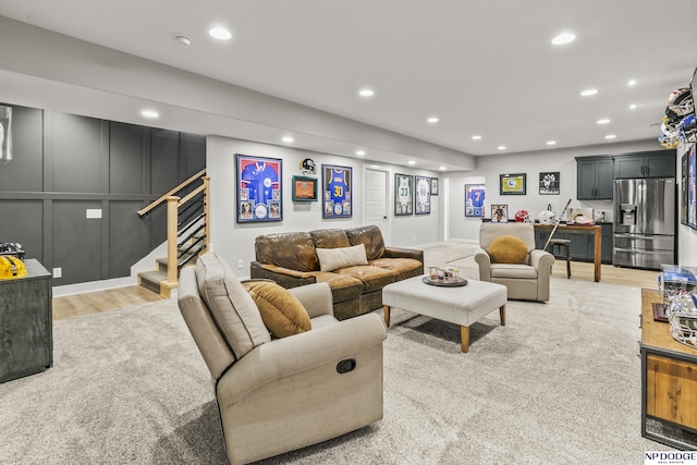 living area featuring light wood-style flooring, recessed lighting, a decorative wall, and stairway