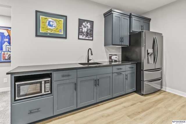 kitchen featuring appliances with stainless steel finishes, dark countertops, a sink, and gray cabinetry