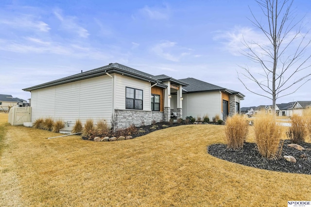 view of front of property featuring a garage, stone siding, roof with shingles, and a front lawn