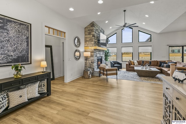 living area with high vaulted ceiling, a fireplace, light wood finished floors, and ceiling fan