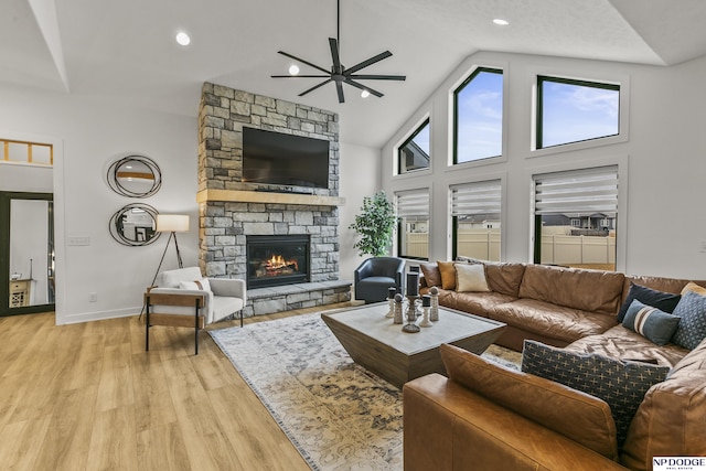 living area with a ceiling fan, a stone fireplace, high vaulted ceiling, light wood-type flooring, and baseboards