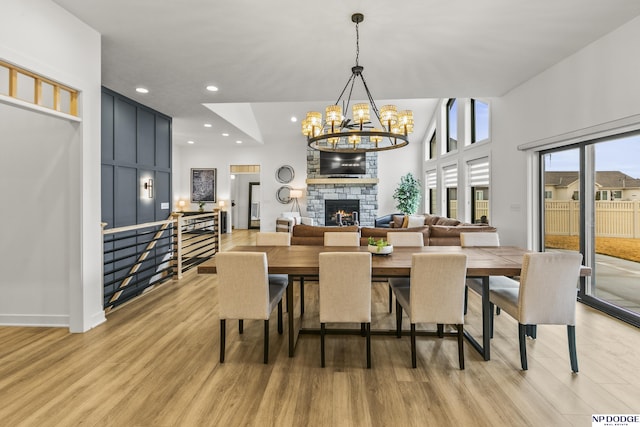 dining room with light wood-style floors, recessed lighting, an inviting chandelier, and a stone fireplace