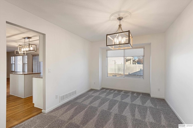 unfurnished dining area featuring baseboards, visible vents, and an inviting chandelier