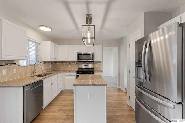 kitchen with light wood-style flooring, a kitchen island, a sink, appliances with stainless steel finishes, and tasteful backsplash