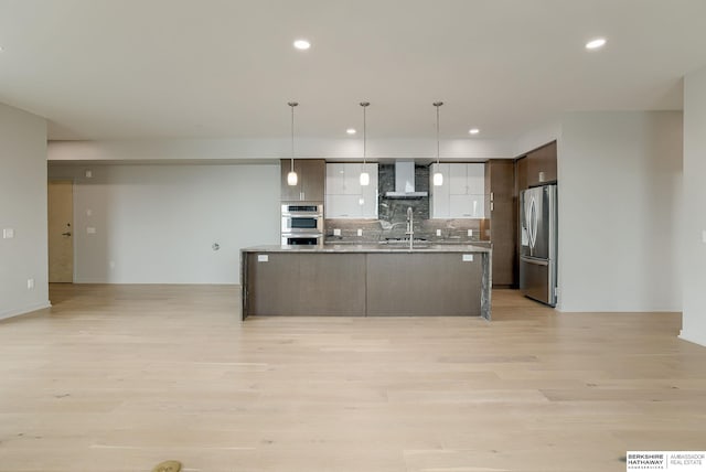 kitchen featuring stainless steel appliances, decorative backsplash, wall chimney range hood, modern cabinets, and light wood-type flooring