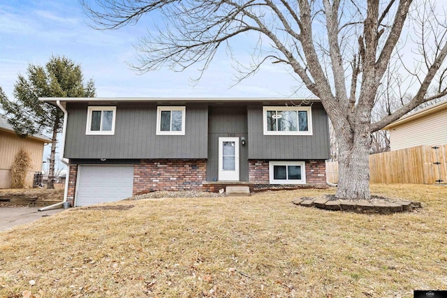 bi-level home featuring a garage, brick siding, a front lawn, and fence