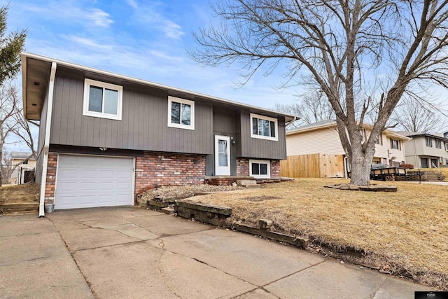 raised ranch with driveway, brick siding, an attached garage, and fence