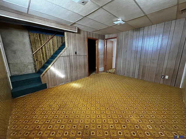 interior space featuring visible vents, wooden walls, a drop ceiling, and stairs