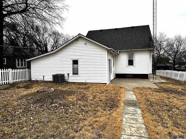 rear view of property with central AC unit, roof with shingles, fence, and a patio