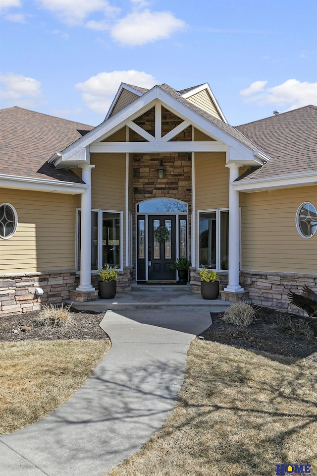 property entrance featuring french doors, stone siding, and roof with shingles