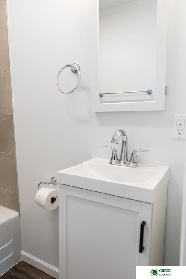 full bath featuring a tub to relax in, vanity, baseboards, and wood finished floors