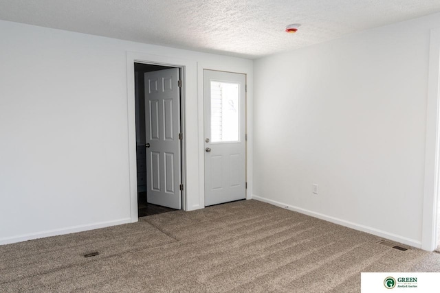 spare room with visible vents, a textured ceiling, baseboards, and carpet flooring