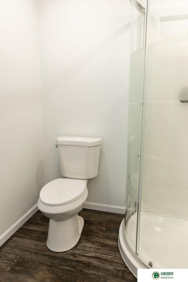 bathroom featuring baseboards, wood finished floors, toilet, and a shower stall