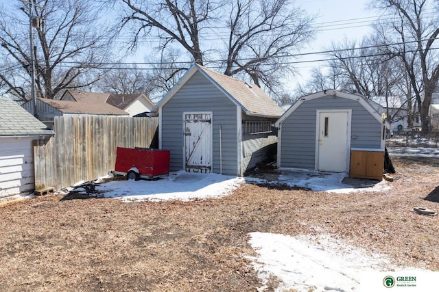 snow covered structure featuring an outdoor structure, fence, and a storage shed