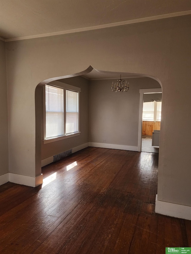 spare room with ornamental molding, arched walkways, dark wood-style flooring, and a notable chandelier