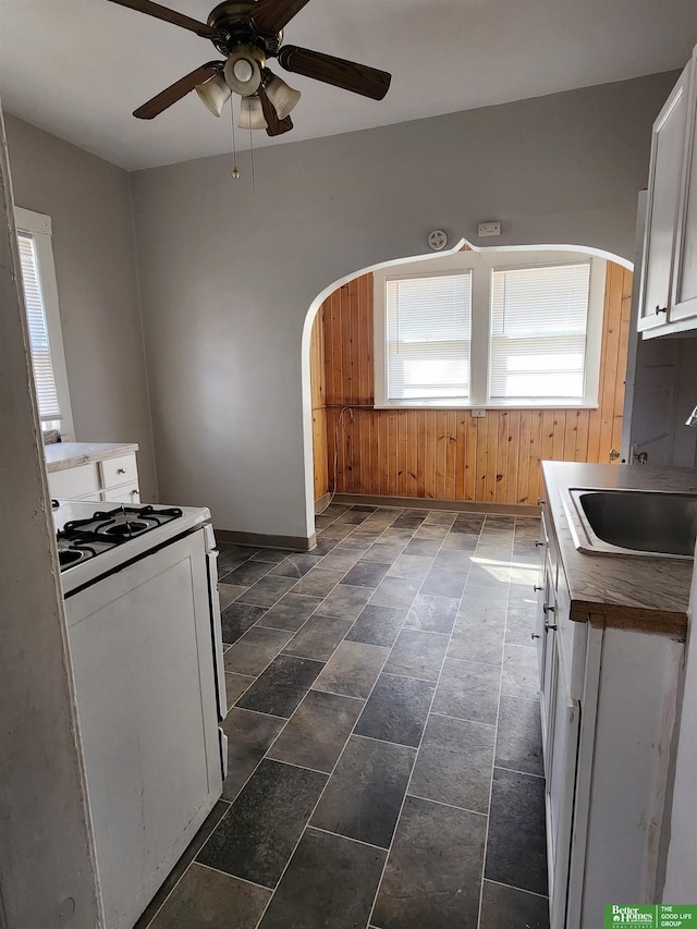 kitchen featuring arched walkways, a sink, a ceiling fan, baseboards, and gas range gas stove