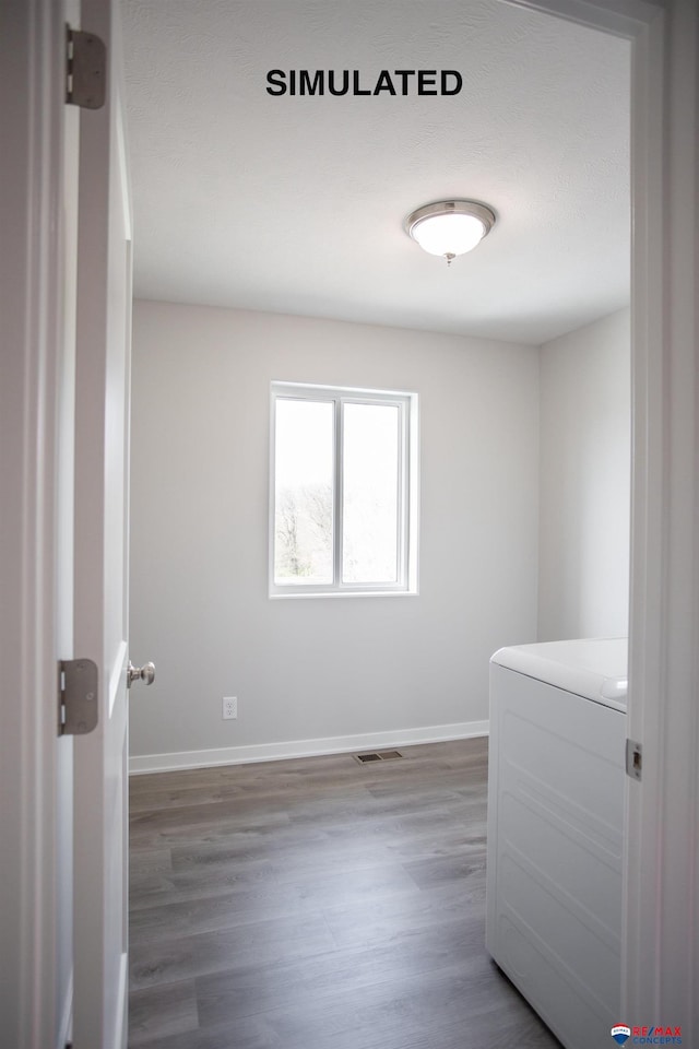 spare room featuring washer / clothes dryer, visible vents, baseboards, and wood finished floors