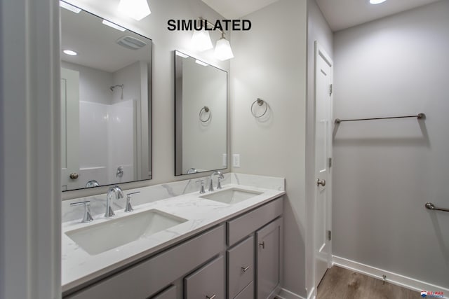 full bath featuring double vanity, wood finished floors, a sink, and baseboards