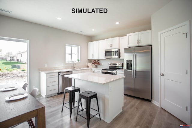 kitchen with a breakfast bar, a kitchen island, a sink, white cabinetry, and appliances with stainless steel finishes