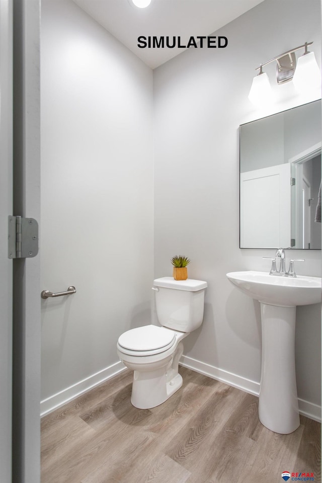 half bathroom with baseboards, toilet, and wood finished floors