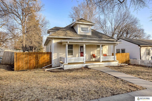 bungalow-style home with a porch, roof with shingles, and fence