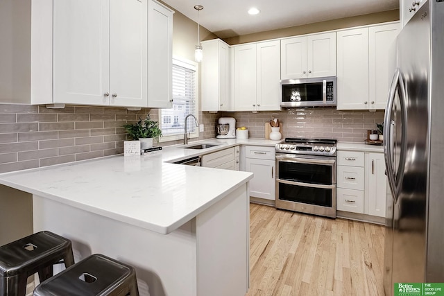 kitchen featuring appliances with stainless steel finishes, a peninsula, light wood-style floors, white cabinetry, and a sink