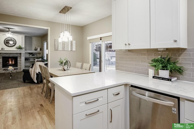 kitchen featuring white cabinets, dishwasher, a stone fireplace, light wood-style floors, and backsplash