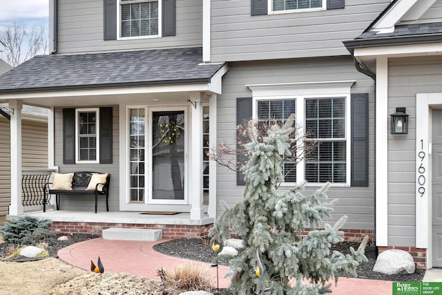 view of exterior entry with covered porch and a shingled roof