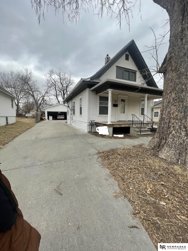 view of front of home with an outbuilding, a porch, a chimney, and a detached garage