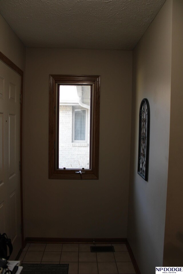 empty room featuring light tile patterned floors, a textured ceiling, visible vents, and baseboards