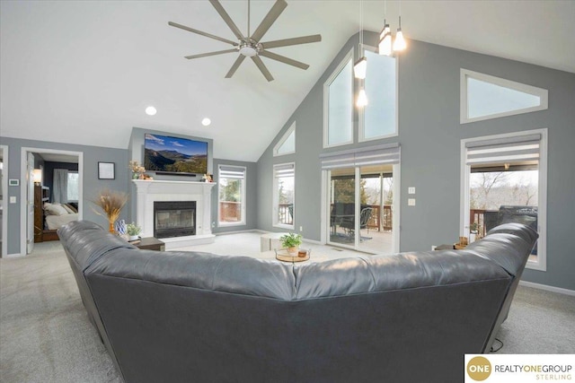 living area featuring high vaulted ceiling, a ceiling fan, a glass covered fireplace, carpet flooring, and baseboards