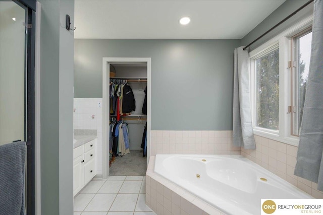 bathroom with tile patterned flooring, vanity, a spacious closet, and a tub with jets