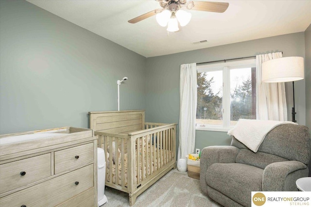 bedroom featuring light carpet, visible vents, ceiling fan, and a nursery area