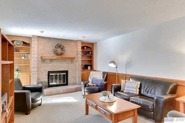 living area with built in features, wainscoting, a textured ceiling, carpet floors, and a brick fireplace