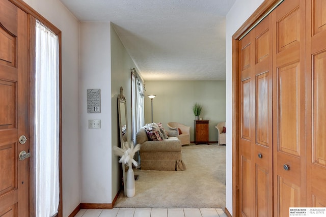 entryway featuring baseboards, light tile patterned flooring, a textured ceiling, and light colored carpet