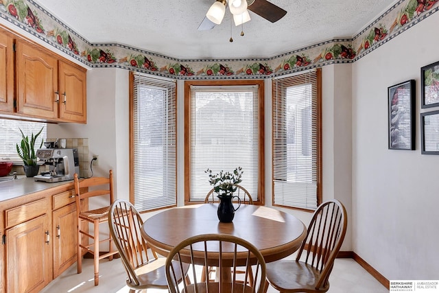 dining room featuring baseboards, ceiling fan, a textured ceiling, and light floors