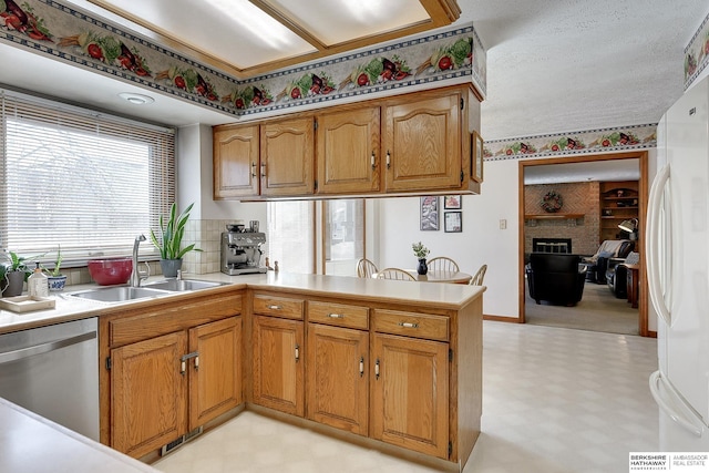 kitchen with dishwasher, freestanding refrigerator, a peninsula, light floors, and a sink