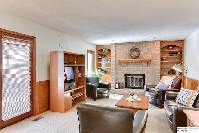 living room featuring visible vents, built in features, light colored carpet, a wainscoted wall, and a brick fireplace