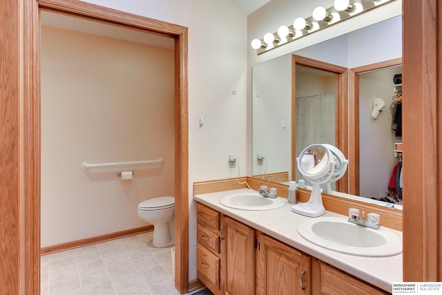 full bath featuring double vanity, a sink, toilet, and baseboards