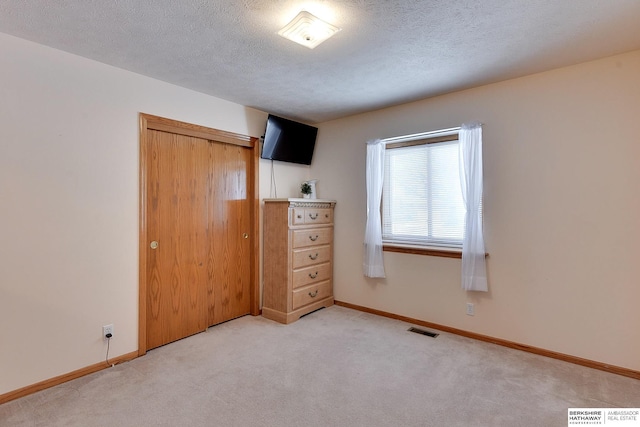 unfurnished bedroom with light carpet, a closet, a textured ceiling, and visible vents