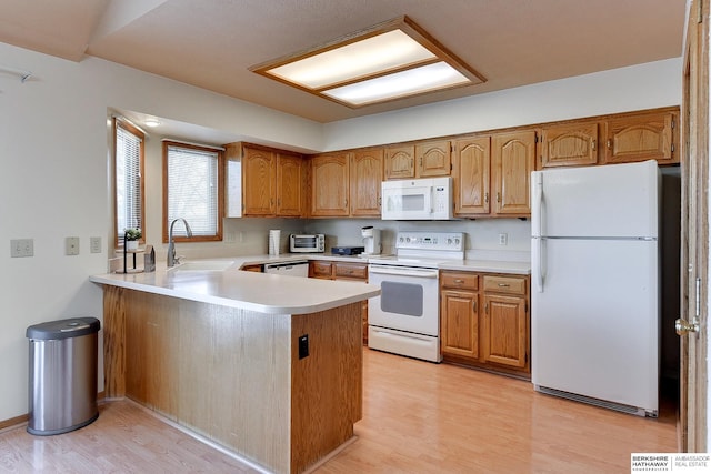 kitchen featuring white appliances, a peninsula, light countertops, light wood-type flooring, and a sink