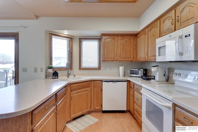 kitchen featuring light wood-style flooring, a peninsula, white appliances, a sink, and light countertops