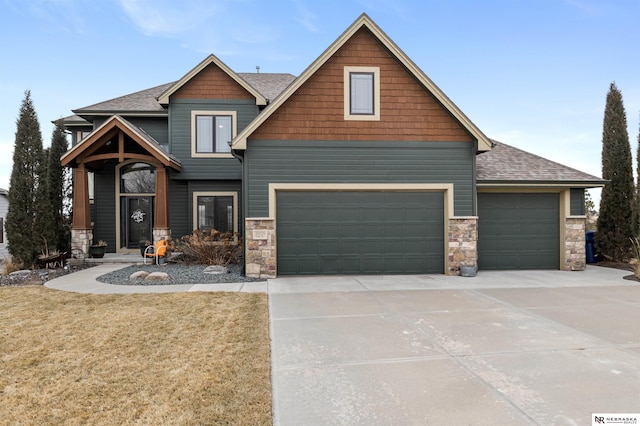 craftsman-style house with an attached garage, a shingled roof, driveway, stone siding, and a front lawn